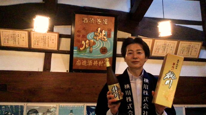 「桃川」の日本酒を持って微笑む営業副本部長の村井さん