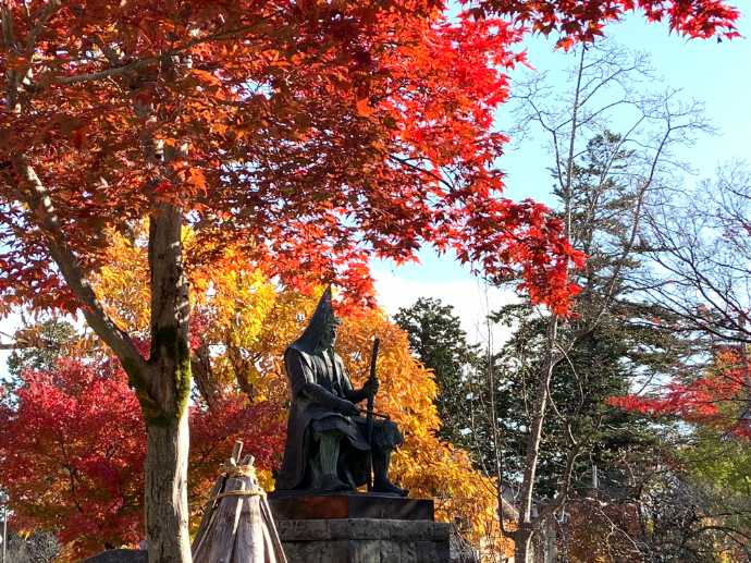 紅葉を背景に撮影した上杉神社にある上杉謙信公の銅像の写真