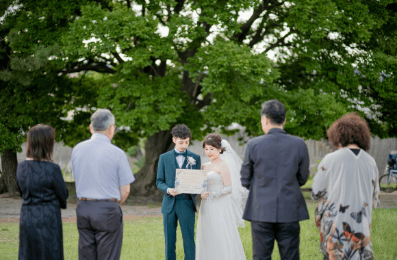 公園にて親族の前で誓いの言葉を読み上げる新郎新婦の写真