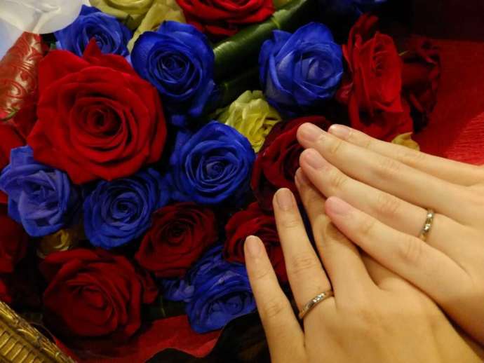 赤や青のバラの前で指輪をした手を重ね合うカップル