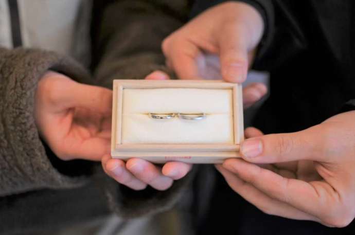 箱に入って納品された結婚指輪を持つカップルの手