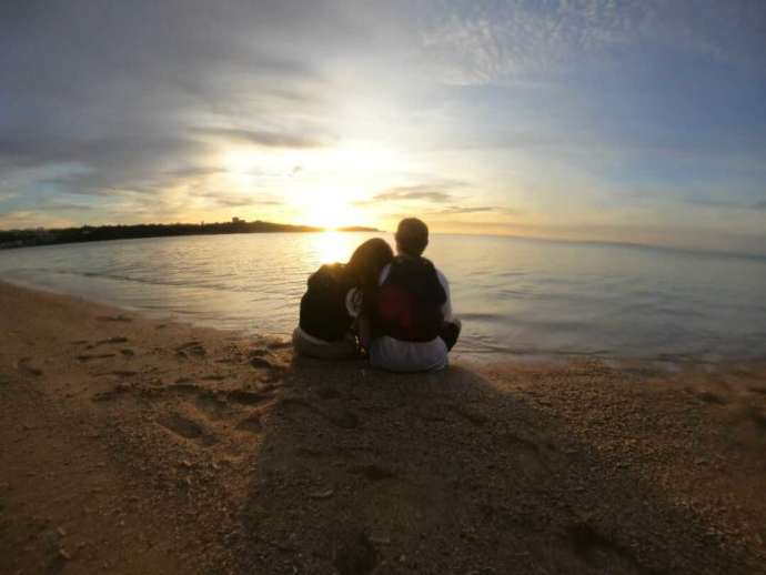 沖縄のビーチで夕陽を見ながら寄り添うカップル