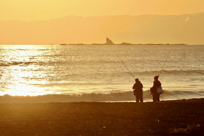 茅ヶ崎市の海岸で夕日を浴びる釣り人と沖合のえぼし岩の図