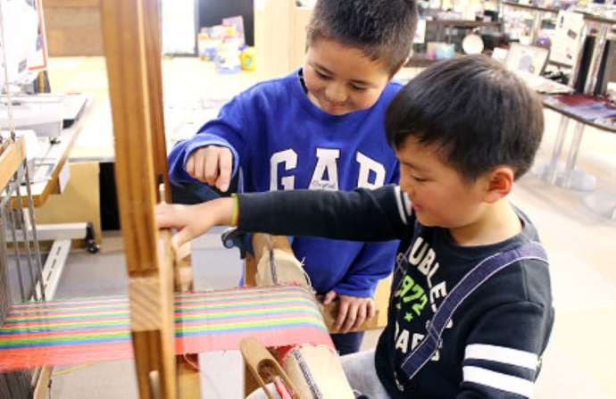 「博多織工芸館（株式会社サヌイ織物）」の手織り体験に参加中の子供たち