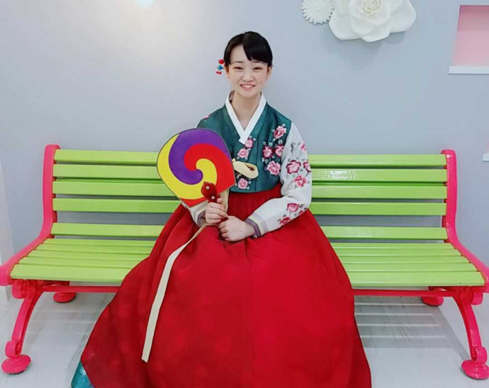 韓国民俗衣装チマチョゴリを着てベンチ座り微笑む女性