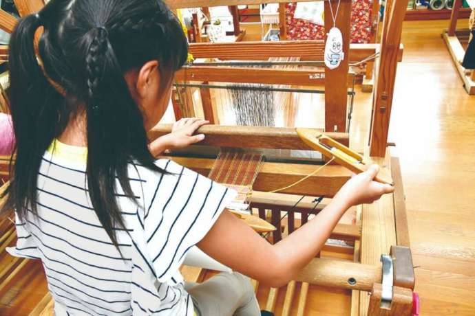 久米島紬の機織り体験をしている子供の様子