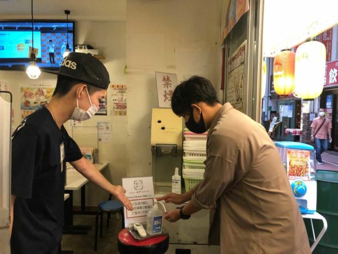 『串カツ田中 大宮店』入り口で消毒を促す店員と消毒中のお客さま