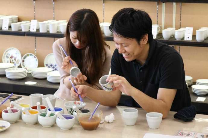 「九谷満月」の陶芸体験「絵付け体験コース」で湯呑に絵付け作業をするカップル