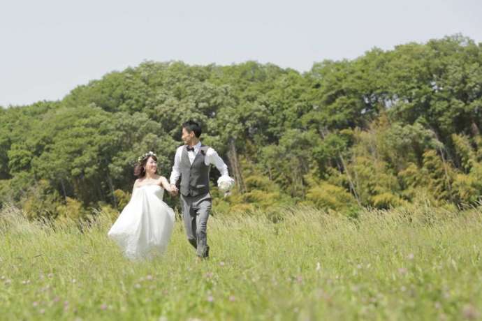 草原の中を手を繋いで走るドレス姿の花嫁と新郎