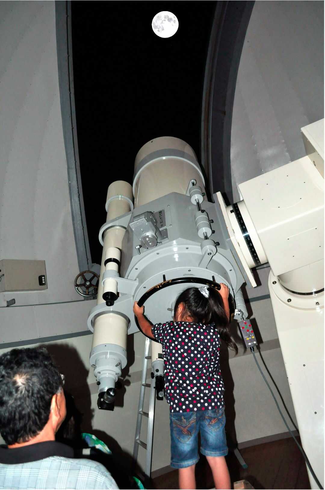 宮崎県都城市にある「たちばな天文台」の大型望遠鏡を覗いて月を眺める子ども