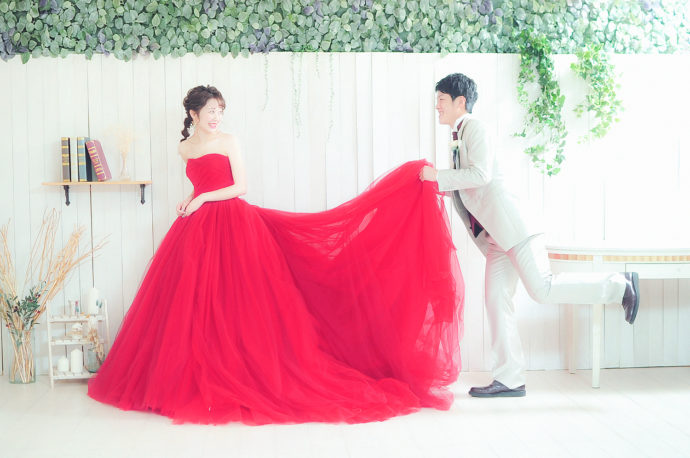 真っ赤なドレスの衣装を来た新婦とドレスの裾を持って笑顔の新郎