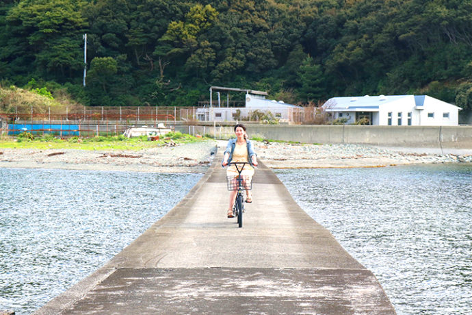 海面すれすれのサイクリングロードを自転車で渡る女性