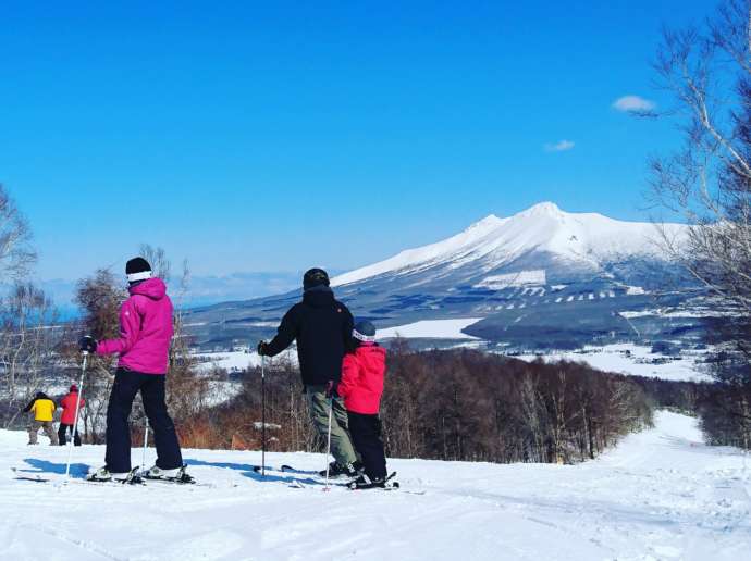 スキー場でスキーをしながら駒ヶ岳を眺める家族