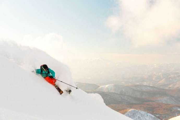 「星野リゾート 猫魔スキー場」の新雪が積もった斜面を滑り降りるスキーヤー