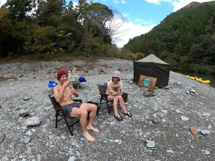 テントサウナ後に河原で飲み物を飲んでリラックスする男性二人
