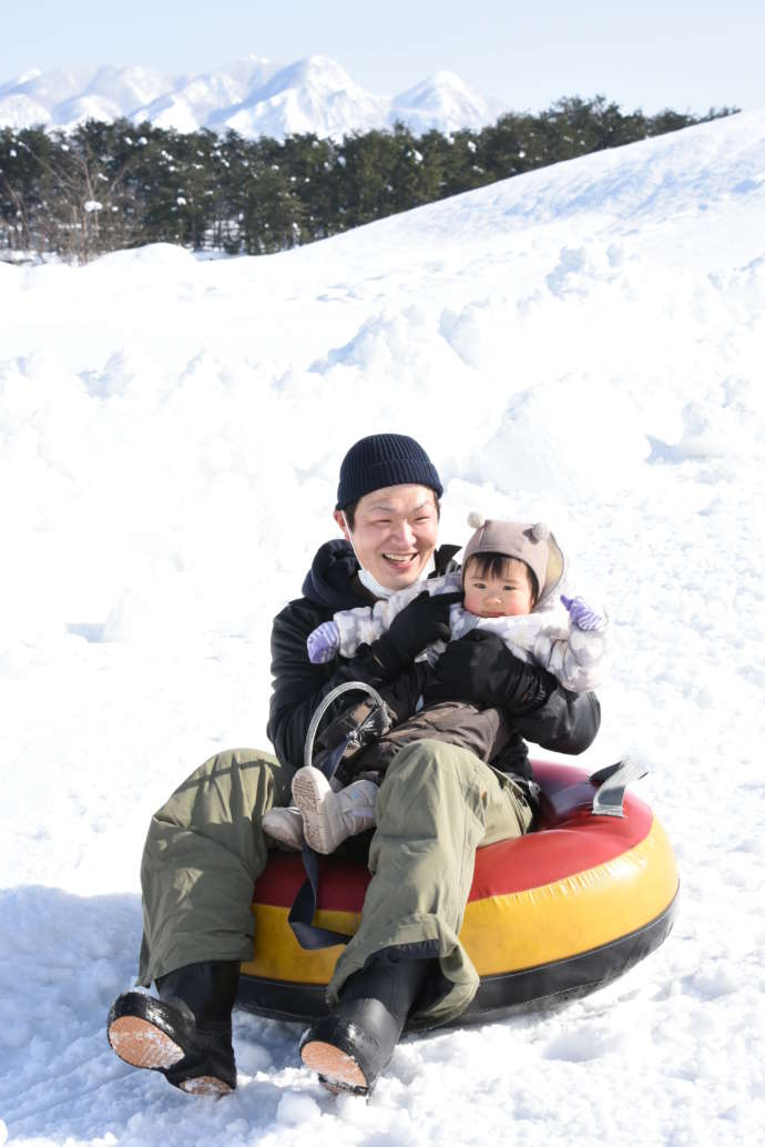 尾花沢市の雪まつりで、ソリ滑りを楽しむ親子