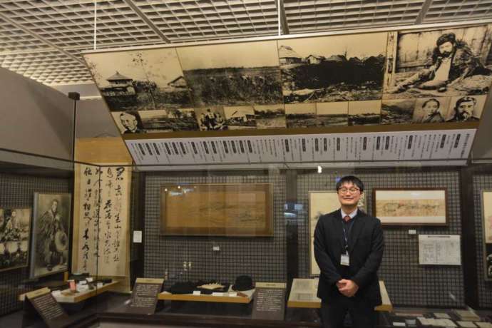 「帯広百年記念館」内に展示される晩成社関連の資料と学芸員の大和田さん（その1）