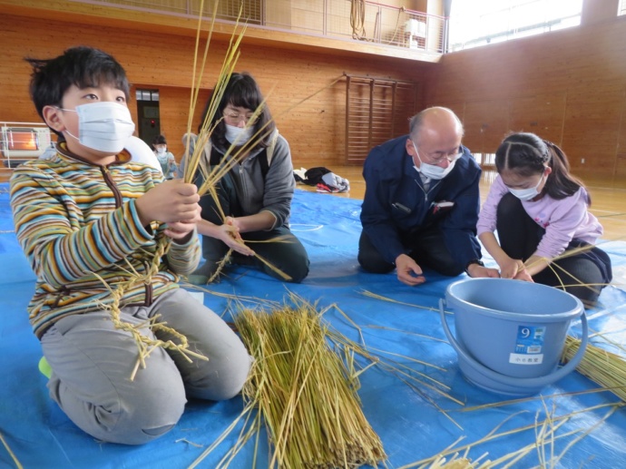 長野県王滝村の小学校で住民と一緒にしめ縄作りをする小学生の写真
