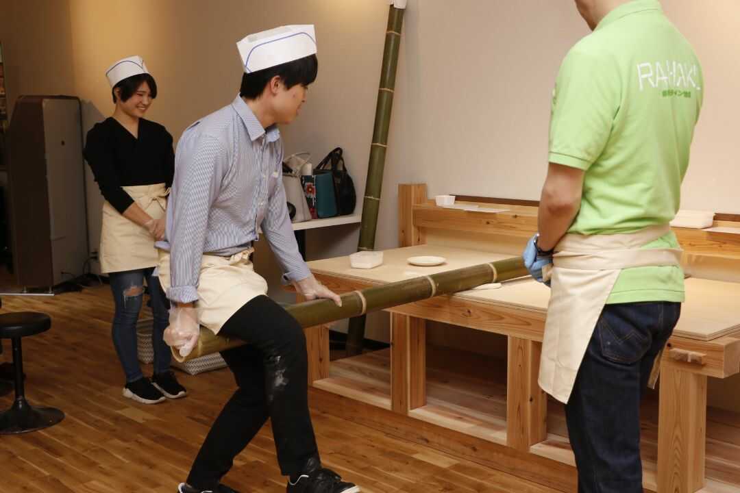 ラーメン作り体験中に竹に自分の体重をかけて麺を伸ばしている様子