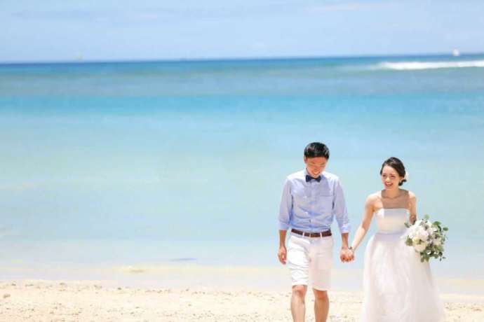ハワイのビーチをバックに手をつないで歩く夫婦