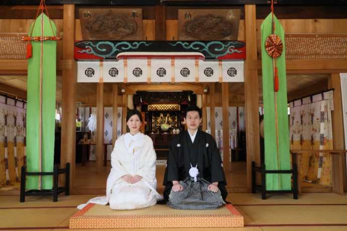 「龍ケ崎 八坂神社」の社殿で記念撮影をする新郎新婦