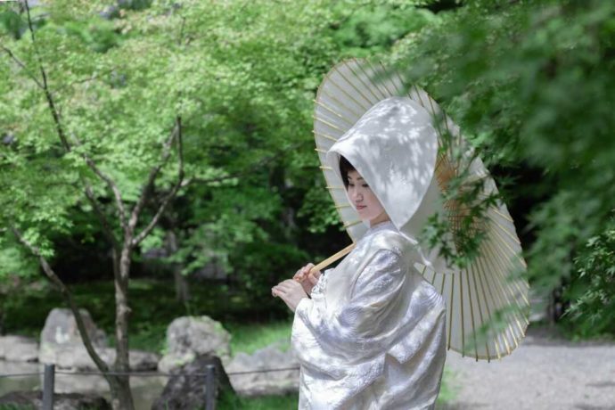 白い番傘をさし庭園に一人佇む白無垢姿の新婦