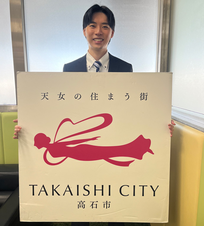 大阪府高石市のキャッチコピーが書かれたボードを持つ男性職員の写真