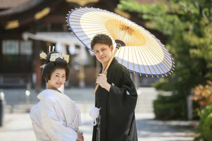 讃岐國一宮田村神社の境内で番傘をさして微笑む新郎新婦