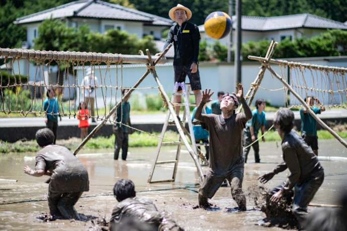 休耕田で泥だらけになってバレーボールをする人々