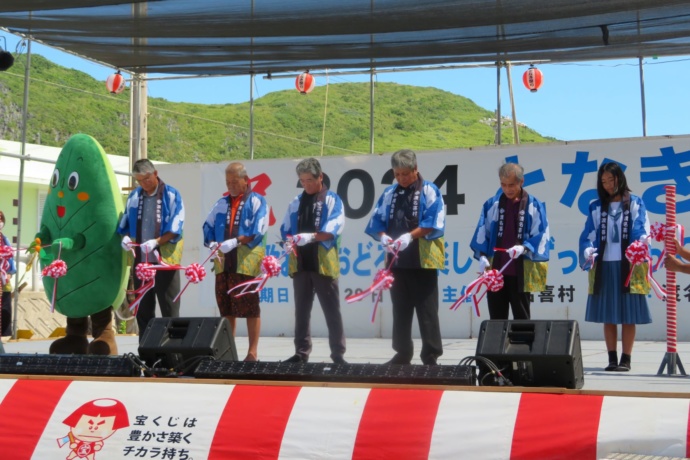 渡名喜村のイベントで村民とふくぎのフーちゃんがテープカットしている様子