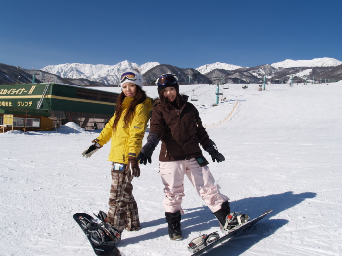 白馬つがいけ高原スキー場のゲレンデで、スノーボードをはいてポーズをとる女性2人の写真