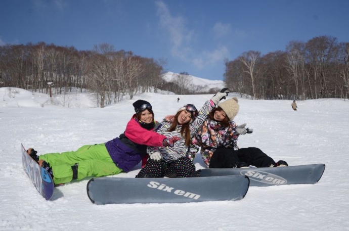 雪上に座ってポーズを決める3人の女性スノーボーダーの写真