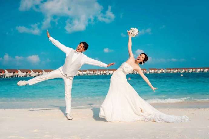 モルディブのビーチで両手を広げてポーズをとる新郎新婦