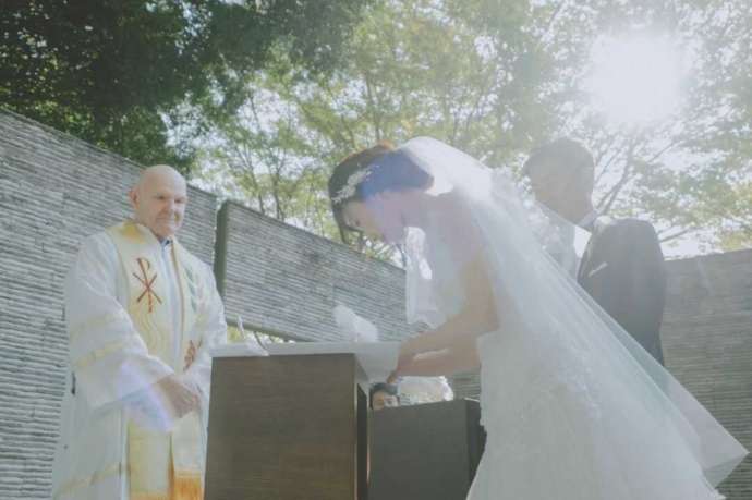 光あふれる屋外チャペルで結婚証明書にサインをする新婦の写真