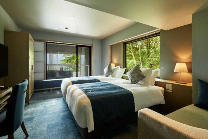 ホテルの部屋、整ったベッド、窓の外に緑の樹木が見える写真