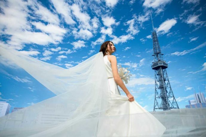愛知県名古屋市にあるテレビ塔を背景に立つウェディングドレス姿の女性