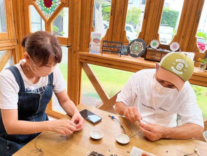 「色伝師 乃和」の「ガラス工芸」制作体験で自分で作ったとんぼ玉をアクセサリーに仕上げているカップル