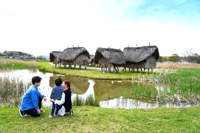 大分県国東市の安国寺集落遺跡公園「弥生のムラ」にある高床建物を引きで眺める家族