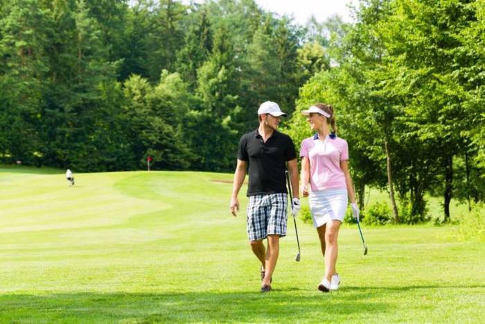 晴れた日にゴルフ場を歩いているカップルの写真
