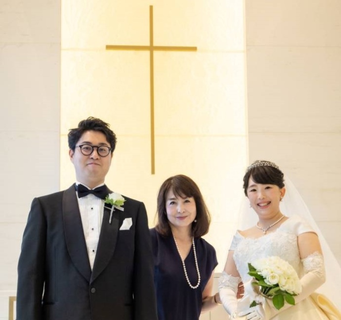 結婚式場で新郎新婦と共に笑顔を見せる大塚さんの写真