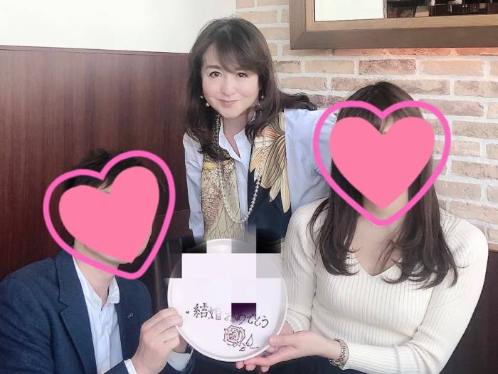 結婚おめでとうの文字が入ったプレートを持つカップルと大塚さんの写真