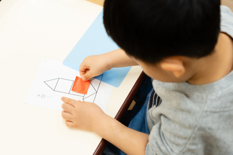 子どもが紙に書かれたロケットの絵の枠に色紙を貼っている様子