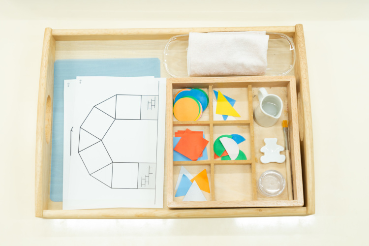 木で作られたケースの仕切りの中に、丸や三角形の色紙、糊、筆が収納されている