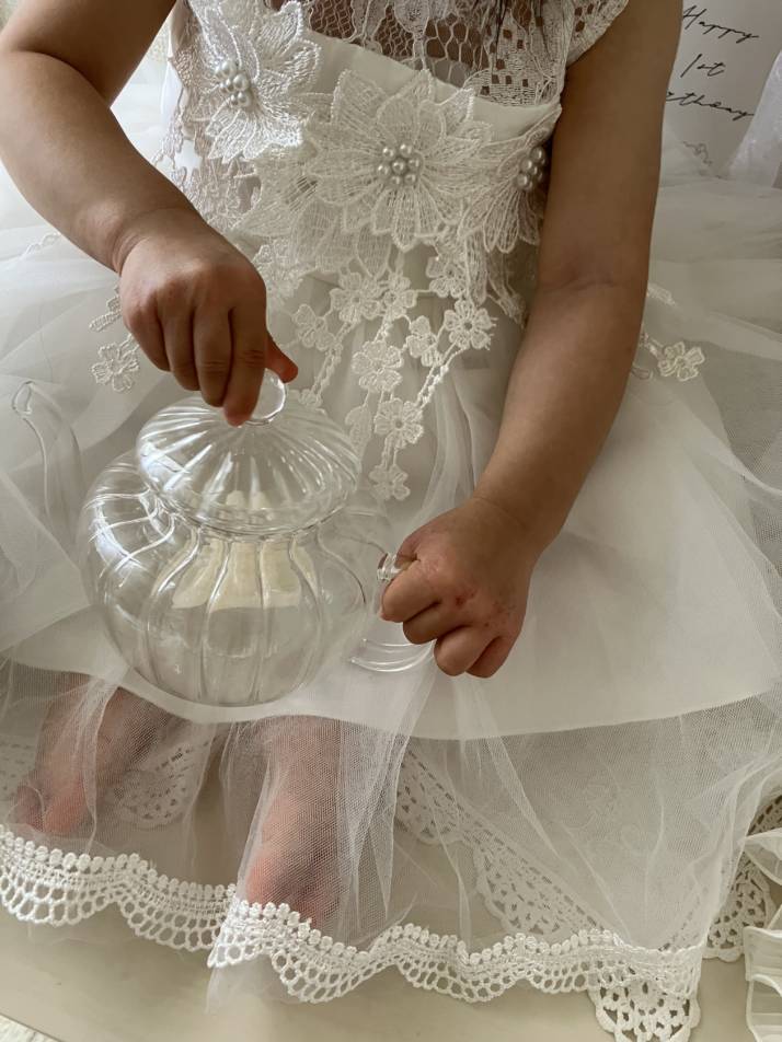 白いドレスを着てガラスのティーポットのふたを開けようとする女の子の写真