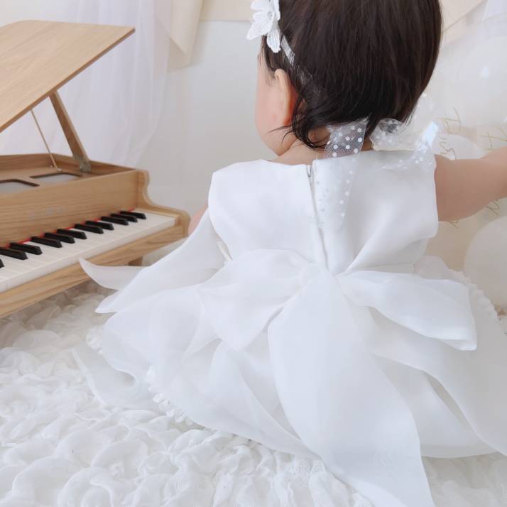 おもちゃの木製ピアノの横でドレスを着て座る赤ちゃんの写真