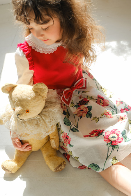 クマのぬいぐるみを抱き寄せる花柄ワンピースの女の子の写真